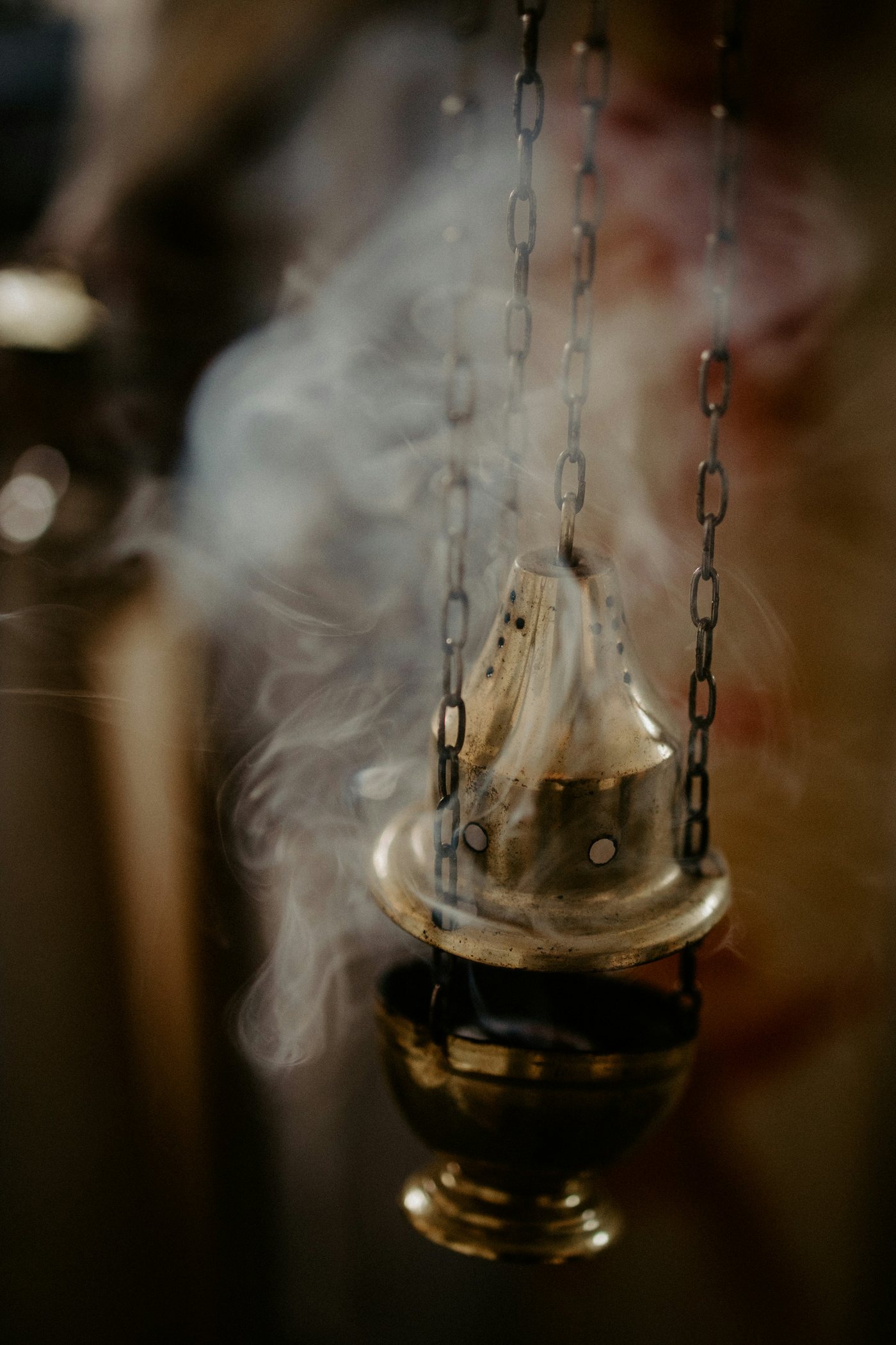 A brass thurible hanging on chains, trailing incense smoke
