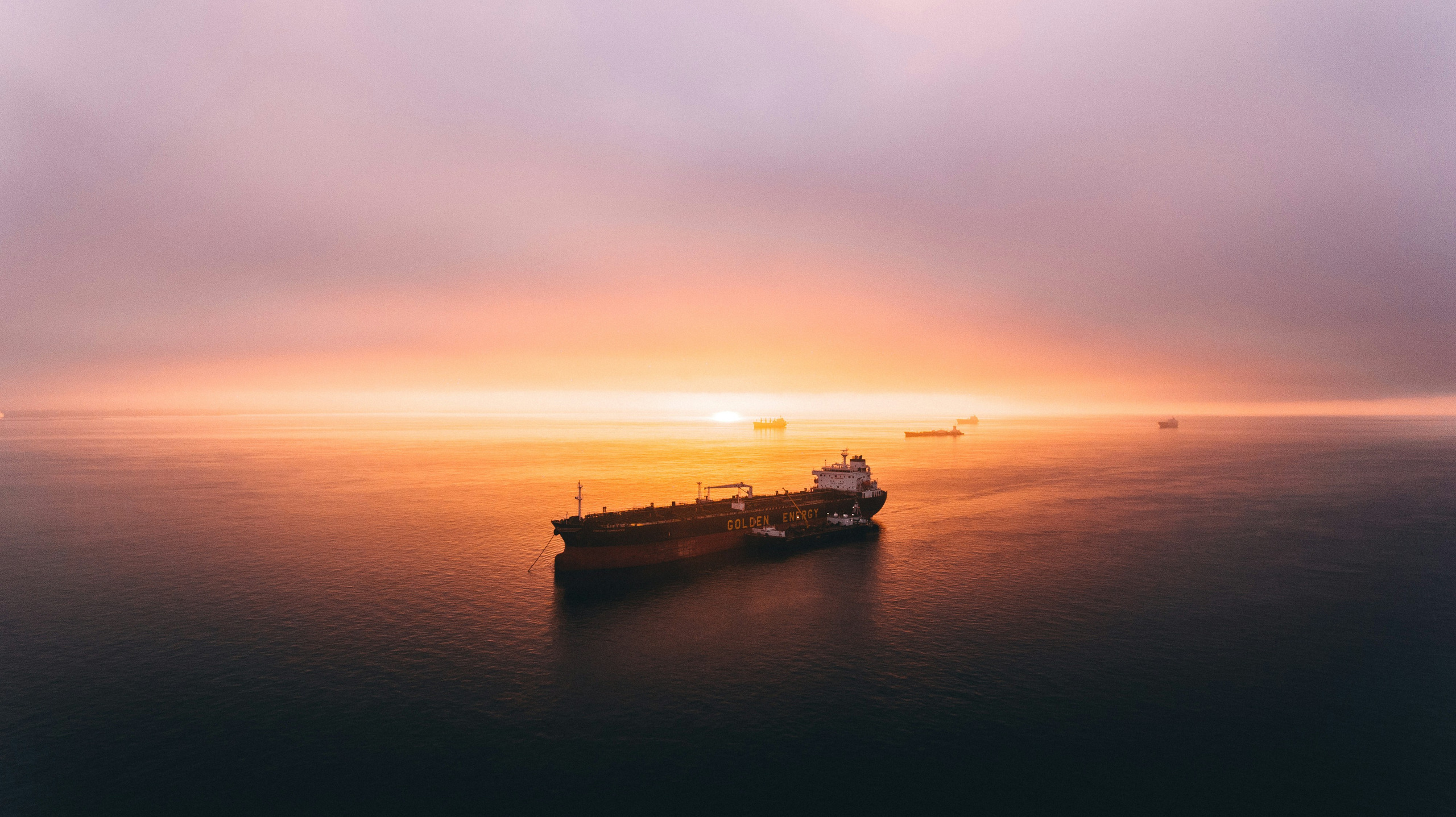 A cargo ship at anchor on calm water at sunset