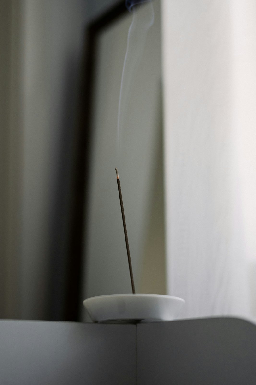 A single stick of incense burning in a white ceramic holder