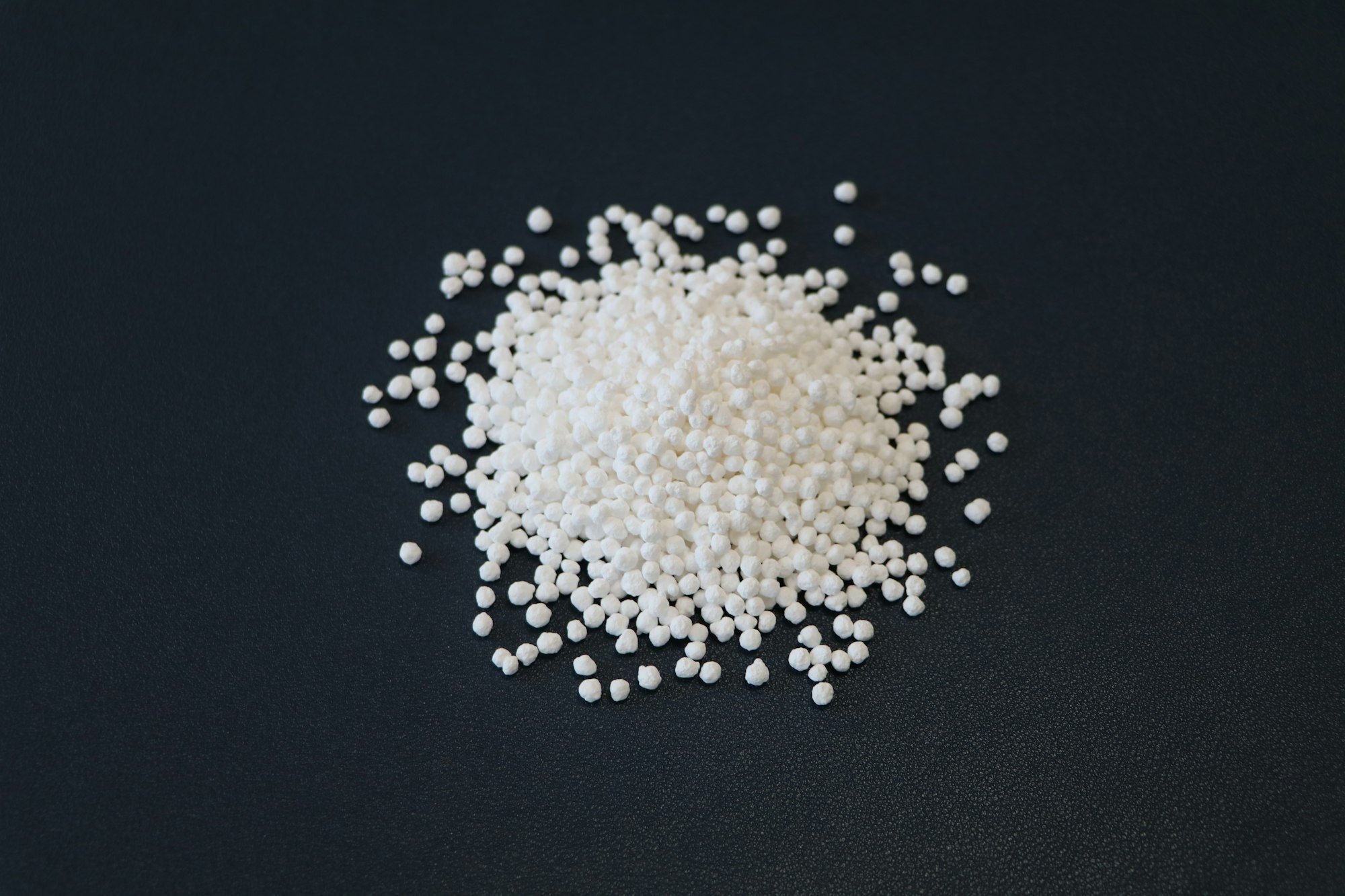 A small pile of white plastic pellets on a dark surface
