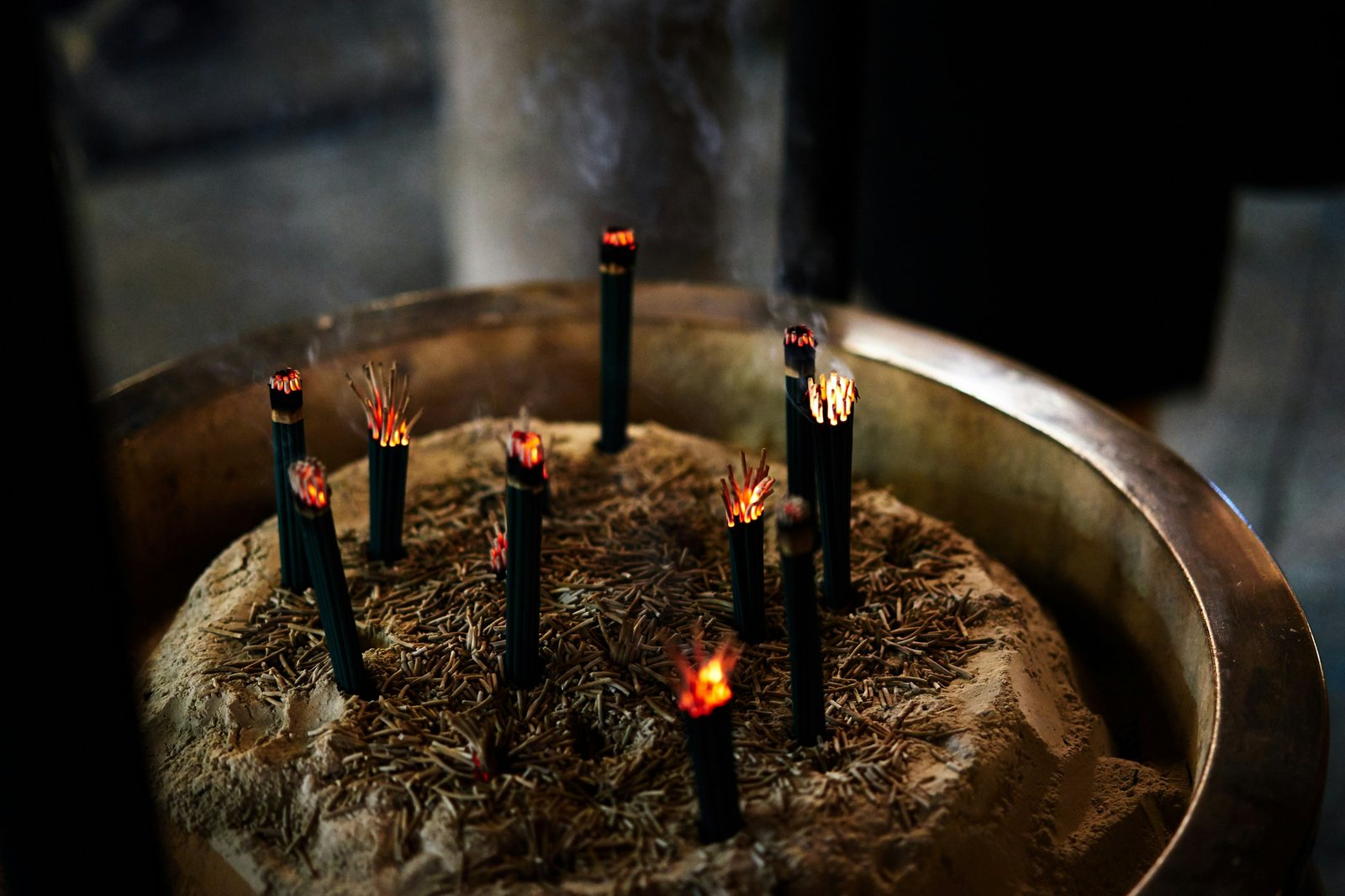 Lit incense sticks standing in a large ash-filled temple burner