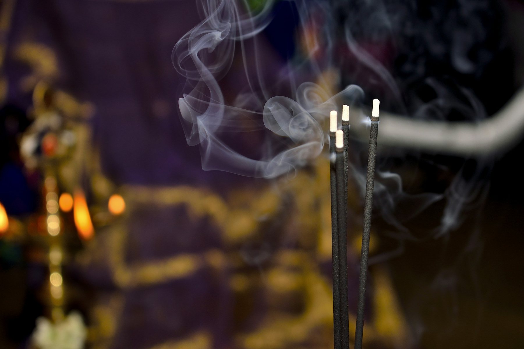 Sticks of incense burning on a Hindu altar beside a brass lamp